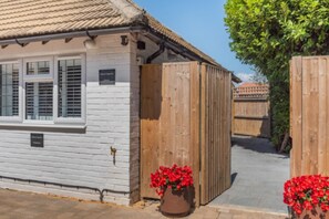 A white building with a tiled roof, a wooden fence, and a potted plant with red flowers. - 1 Bed in Yapton (oc-b32757) (Yapton)