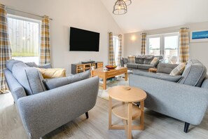 A modern living room with grey sofas, a wooden coffee table, and a flat-screen TV mounted on the wall. - 4 Bed in Padstow (oc-r32776) (Padstow)