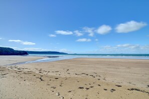 Ein weiter Sandstrand mit sanften Wellen, einem klaren Himmel und Hügeln in der Ferne.
