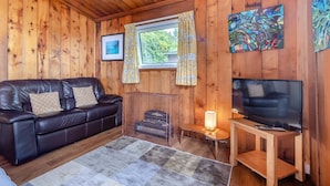 A cozy cabin interior with a leather sofa, a television, wooden walls, a window with curtains, and a painting. - 3 Bed in Broad Haven (oc-wav604) (Haverfordwest)