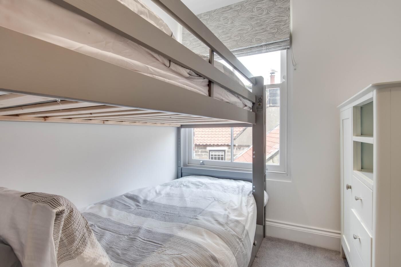 Un letto a castello con una finestra, un comò e un termosifone.