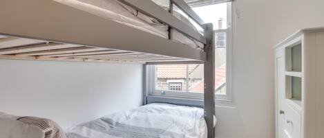 Un letto a castello con una finestra, un comò e un termosifone.