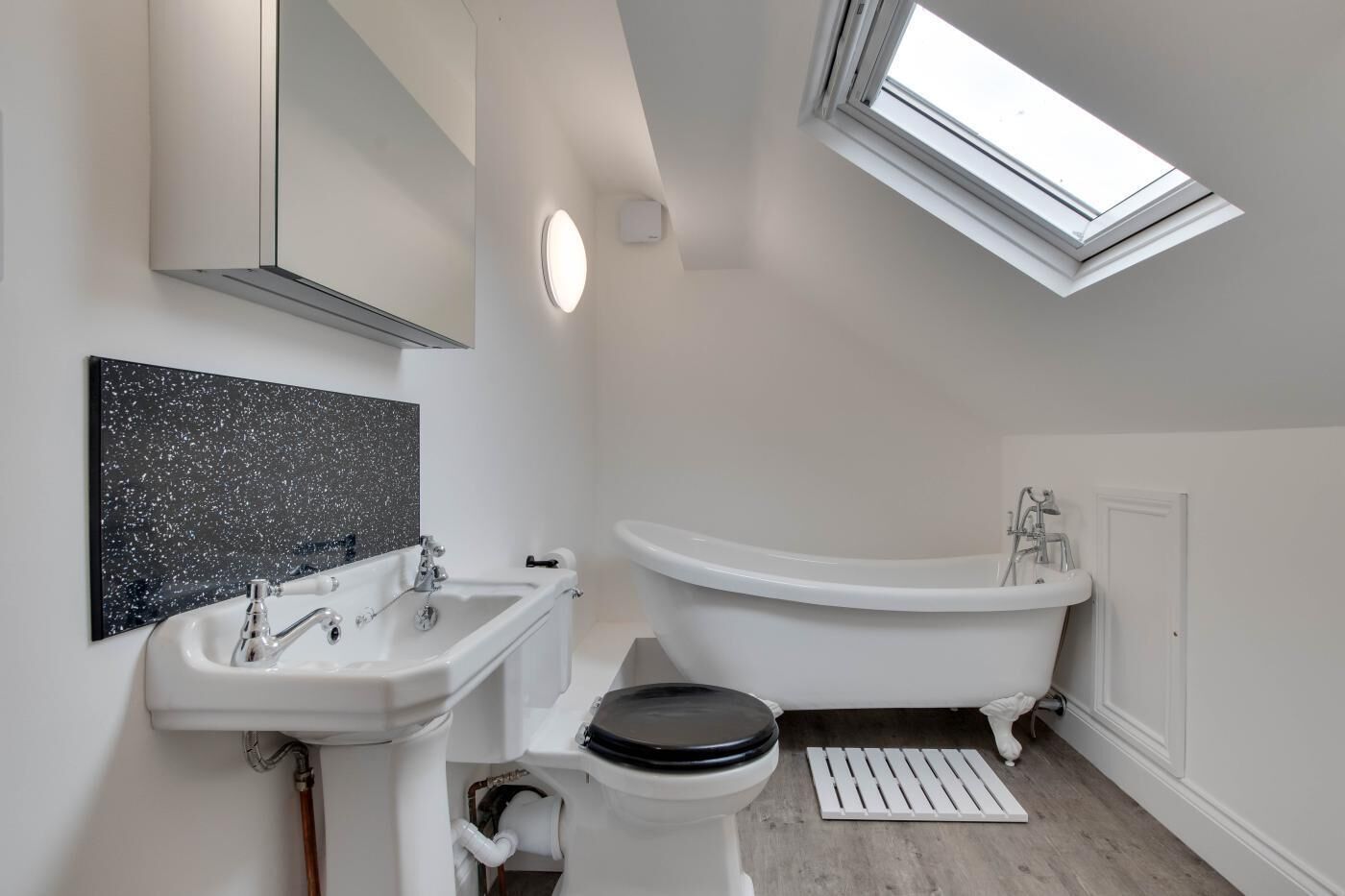 Un baño moderno con tragaluz, una bañera independiente, un lavabo y un inodoro.