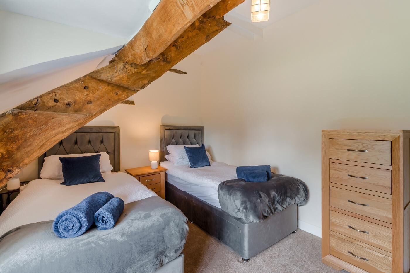 A bedroom with two beds, a wooden dresser, and a sloped ceiling with exposed beams.