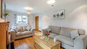 A living room with two sofas, a coffee table, a wooden cabinet, a window with curtains, a door, and a wall-mounted artwork. - 2 Bed in Pickering (oc-d32743) (Pickering)