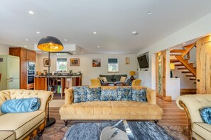A spacious living area with a sofa, armchairs, a coffee table, and a dining area with a kitchen in the background. - 3 Bed in Birnam (oc-o32901) (Birnam)