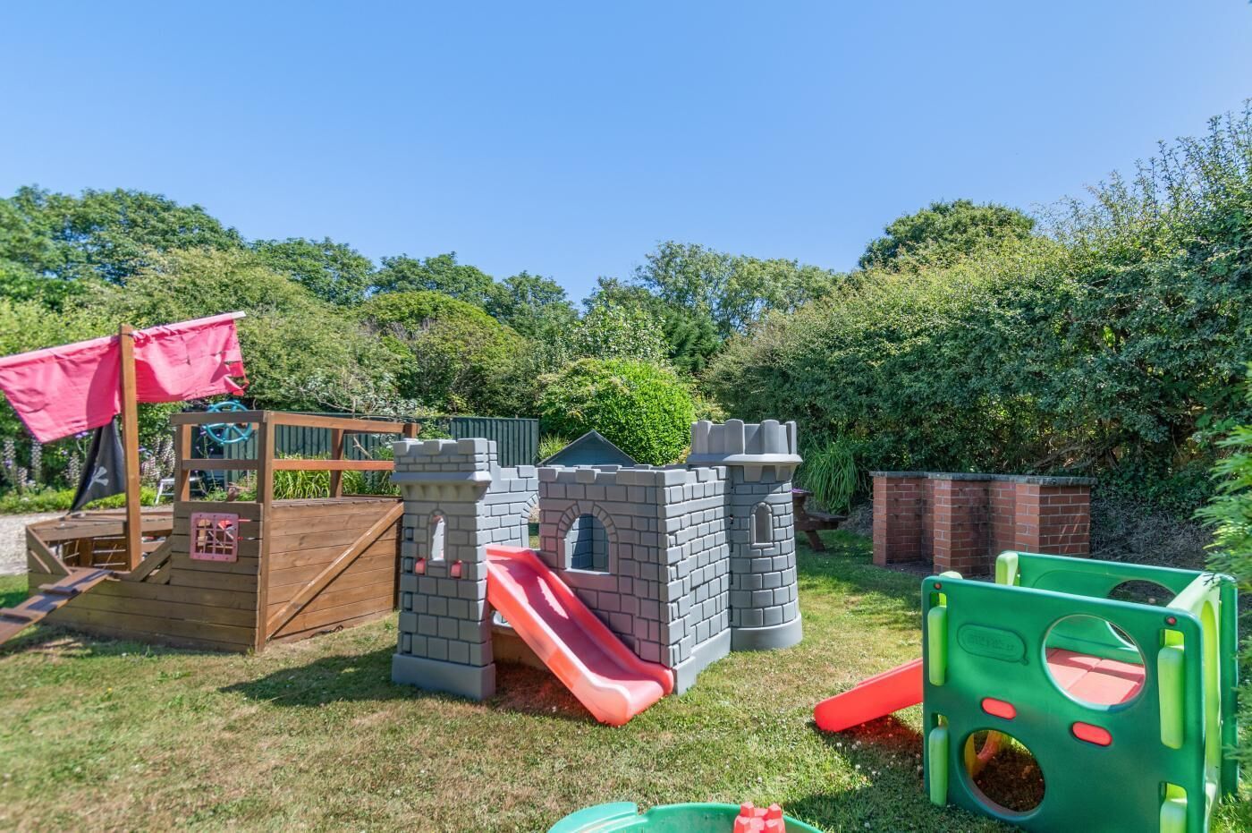 A children's play area with a wooden playhouse, a brick castle, and a slide.