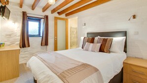 Ein Schlafzimmer mit Bett, Holz-Kopfteil, weißer Ziegelwand und einem Fenster mit Vorhängen.
