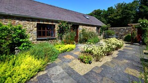 Ein Haus aus Stein mit einem geneigten Dach, einer Steinfassade und einem Garten mit gelben Blumen und Sträuchern.