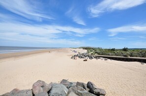 A wide sandy beach with a wooden boardwalk, rocky outcrops, and sparse vegetation. - 3 Bed in Brancaster (oc-2153) (Brancaster)
