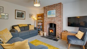 A living room with a fireplace, sofa, bookshelf, and television. - 3 Bed in Brancaster (oc-2153) (Brancaster)