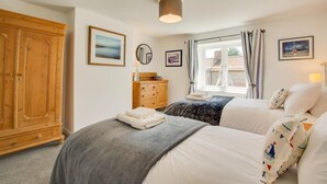 A bedroom with two beds, a wooden wardrobe, a dresser, and a window with curtains. - 3 Bed in Brancaster (oc-2153) (Brancaster)