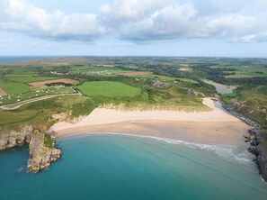 Eine Luftaufnahme einer Küstenlandschaft mit Sandstrand, felsiger Küste und grünen Feldern.