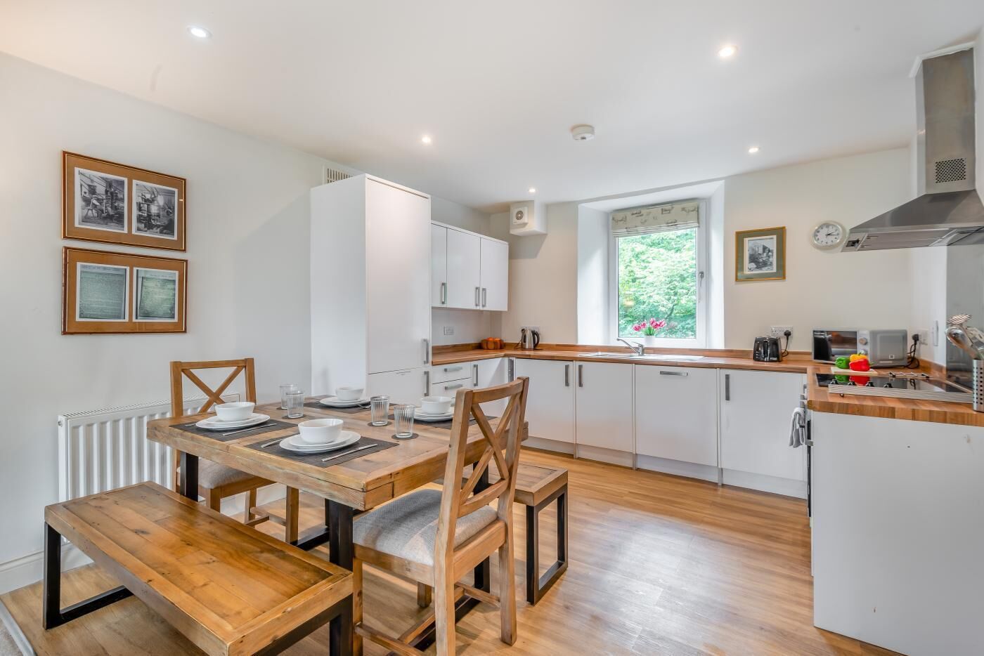 A modern kitchen with white cabinets, a wooden dining table, and a window providing natural light.