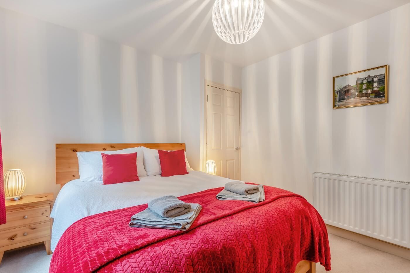 Ein Schlafzimmer mit einem hölzernen Bett, weißer und roter Bettwäsche, einer roten Steude und einem Heizkörper.