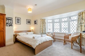 A bedroom with a large bed, two chairs, a window with curtains, and framed pictures on the wall. - 4 Bed in Tenby (oc-pw500a) (Tenby)