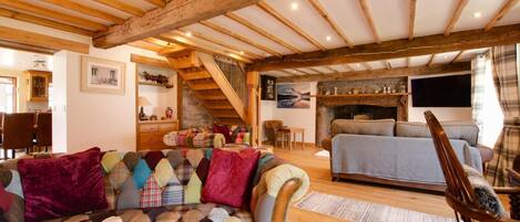 A cozy living room with a large, colorful sofa, a wooden ceiling, and a fireplace.