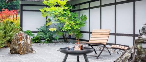 Una fogata con una silla y una roca grande en un jardín, con un edificio al fondo.