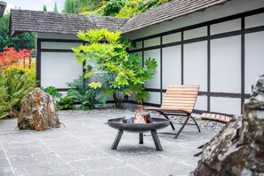 A fire pit with a chair and a large rock in a garden area with a building in the background. - 1 Bed in Tollard Royal (oc-j32937) (Tollard Royal)