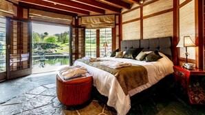 Un dormitorio amplio con una cama grande, techo de madera y vistas a un jardín a través de ventanas amplias.