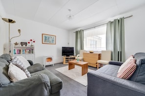 A living room with a sofa, TV, bookshelf, and a fireplace. - 1 Bed in Tenby (oc-pw983a) (Tenby)