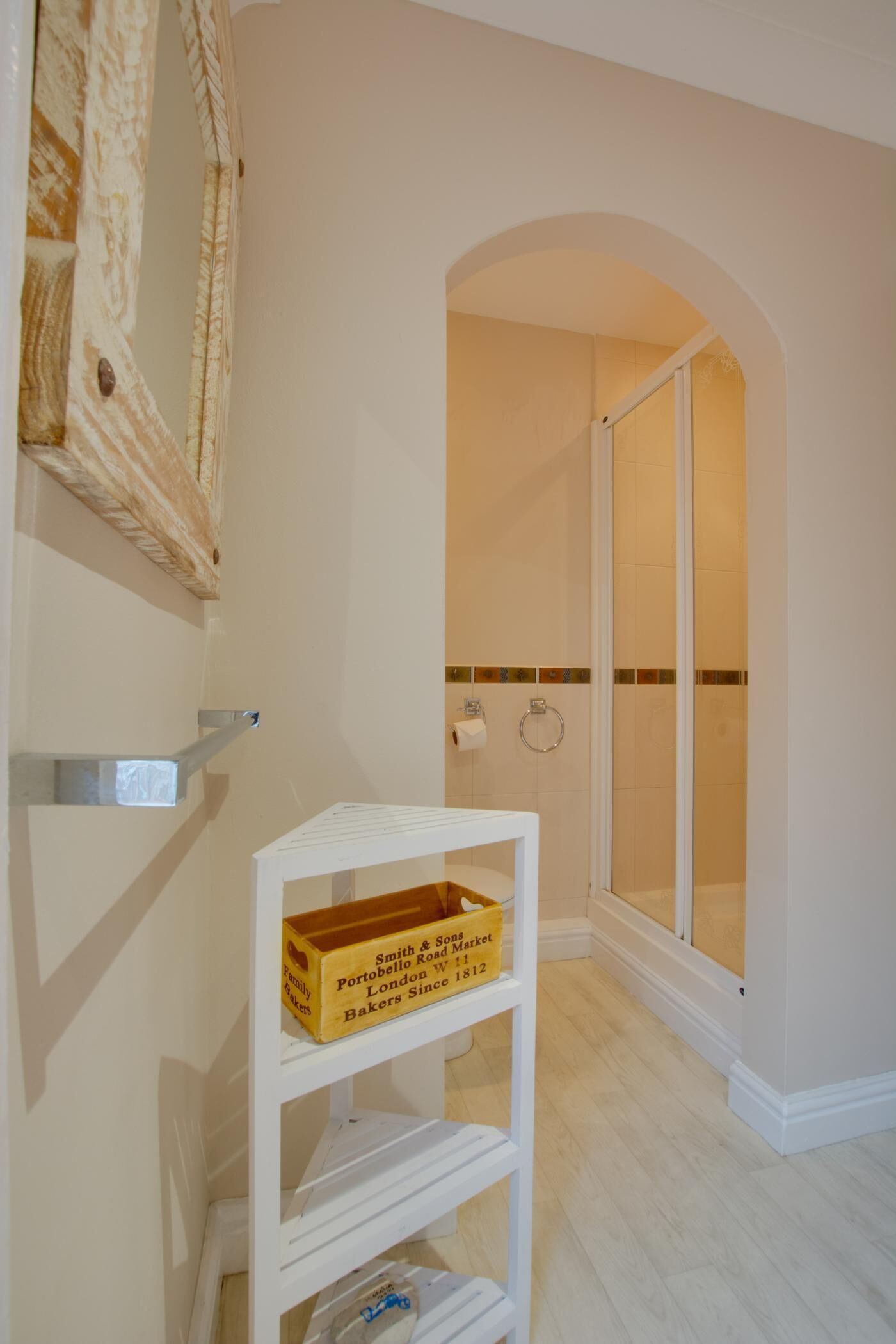 Ein Badezimmer mit Dusche, einem weißen Regal mit einer Schachtel, auf der 'Smith & Sons Portobello Road London Since 1812' steht, und einer gefliesten Wand.