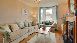 A living room with a beige sofa, a coffee table, and a fireplace. - 3 Bed in Heacham (oc-2203) (Heacham)