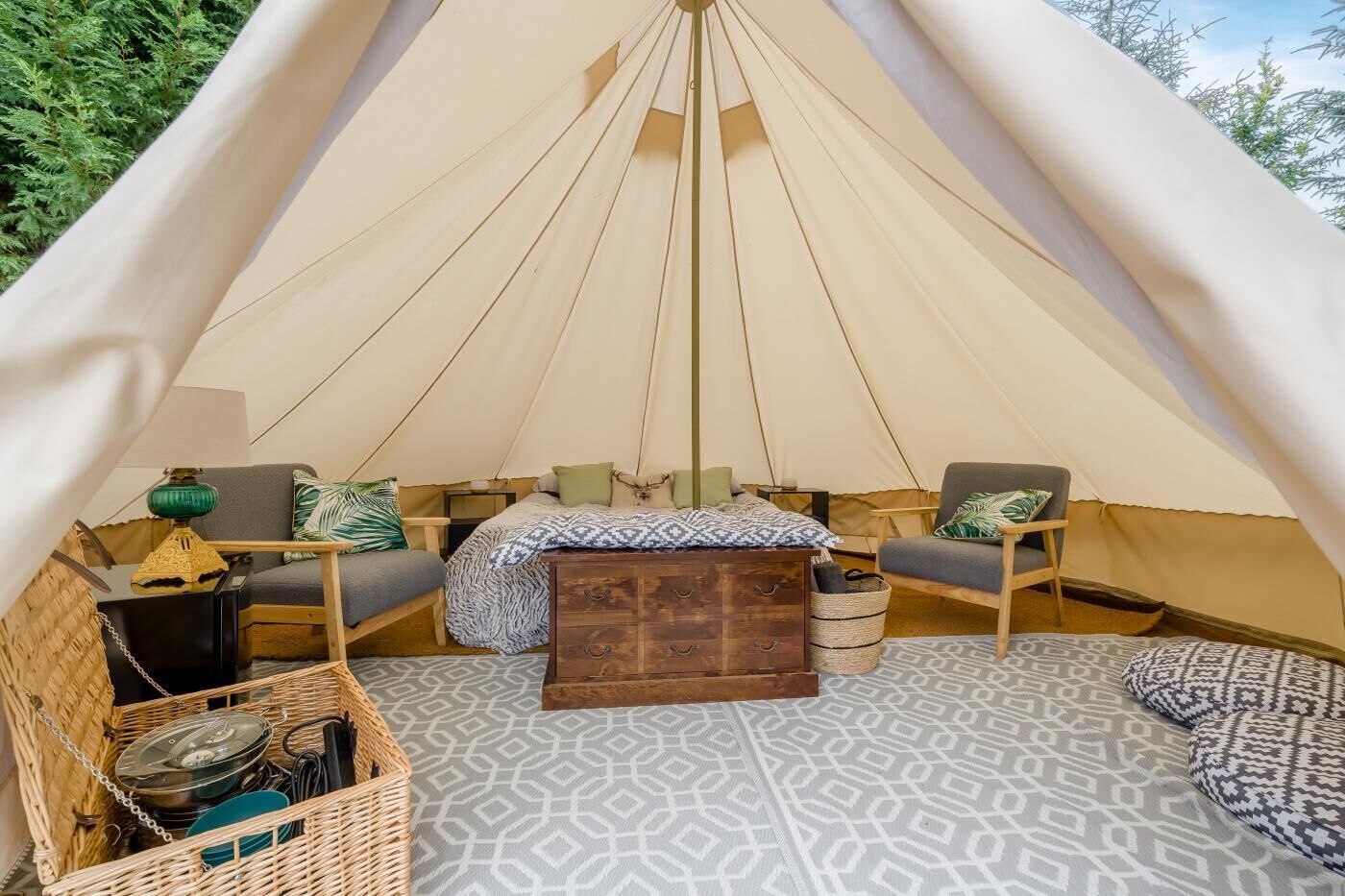 A cozy tent interior with a bed, two chairs, a small table, and a storage chest.