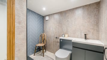A bathroom with a shower, a toilet, a sink, and a chair.