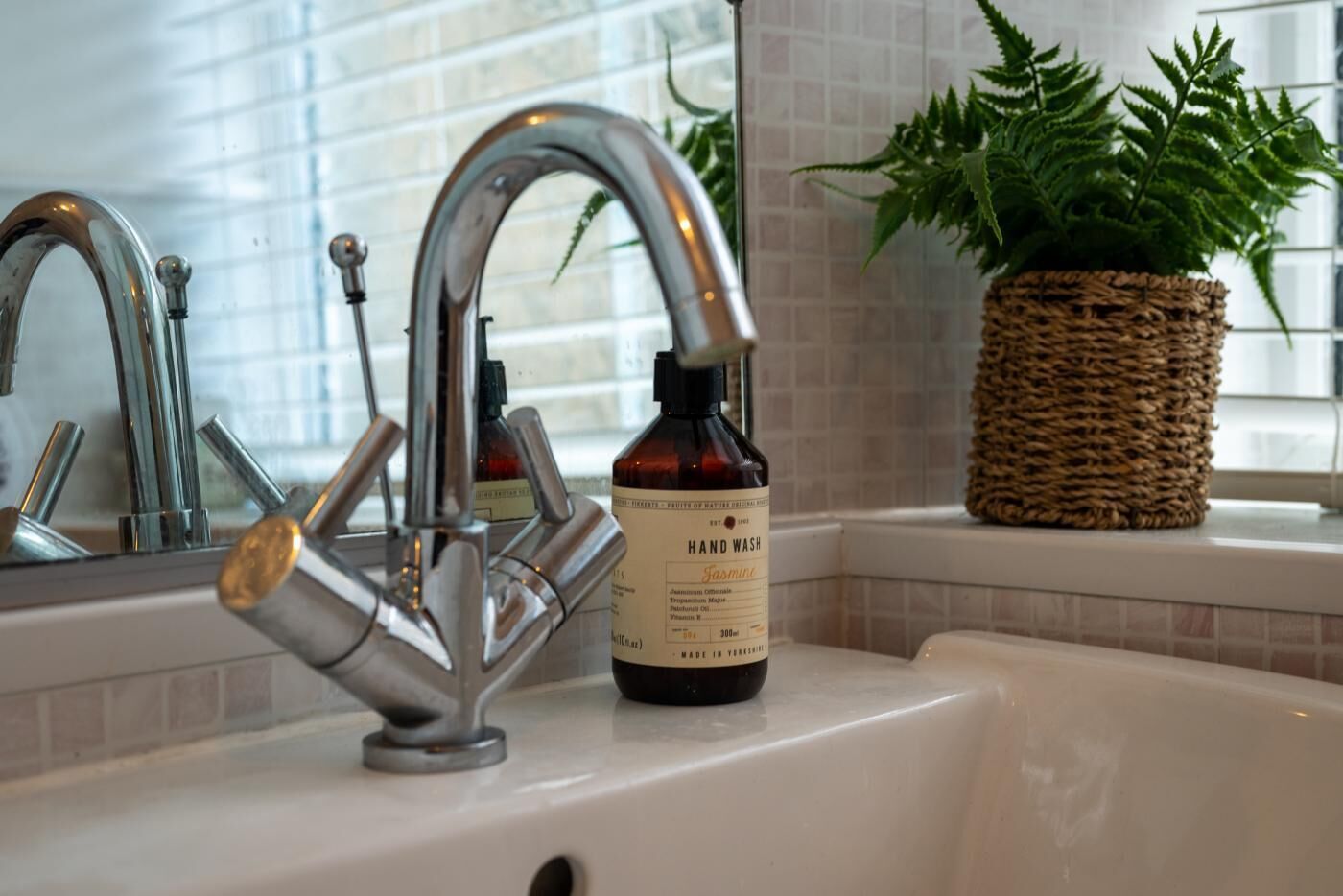 Un lavabo de salle de bain avec un robinet moderne, un flacon de savon liquide et un panier en osier contenant une plante.