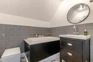 A modern bathroom with a bathtub, a vanity with drawers, a toilet, and a round mirror on the wall. - 5 Bed in Bodham (oc-2204) (Bodham)
