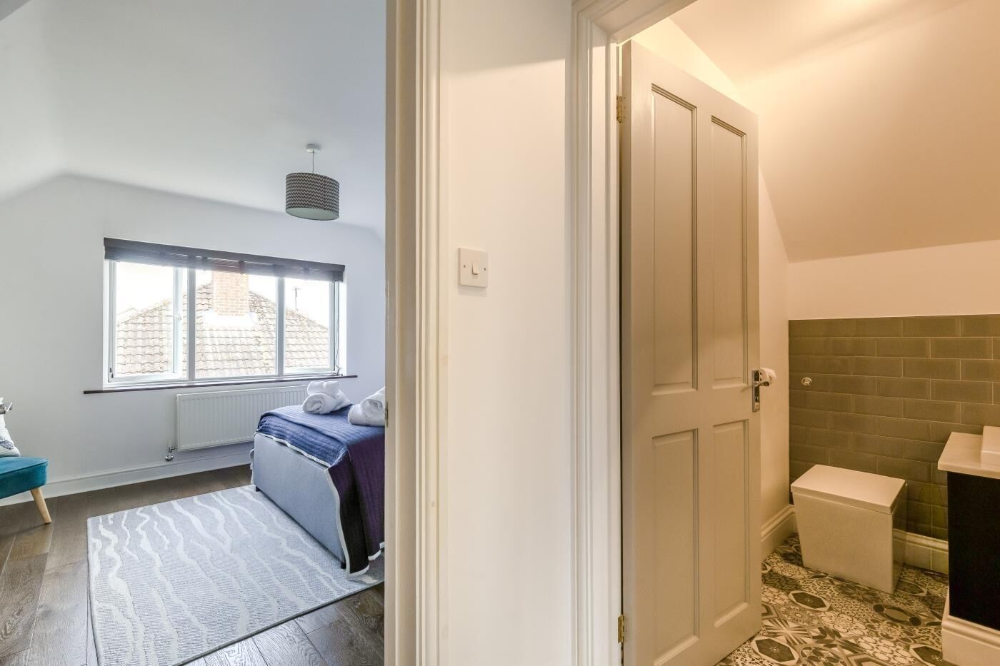 A bedroom with a bed, a window, a radiator, and a bathroom with a sink and toilet.