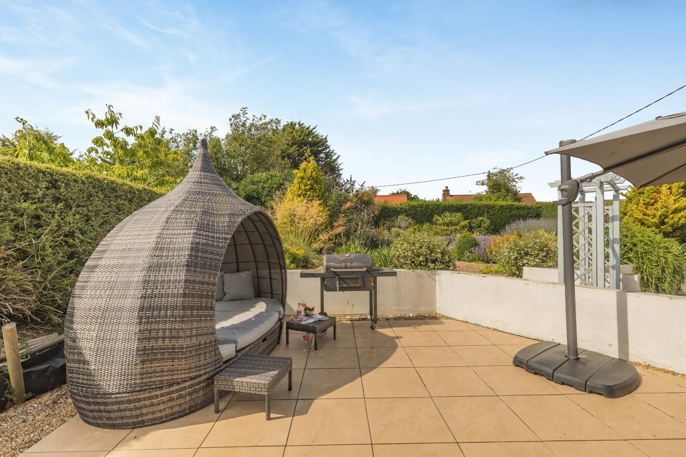 Een terras met een geweven zithoek, een barbecue en een pergola.