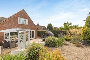 A brick house with a patio, outdoor seating, and a garden with various plants and a decorative stone feature. - 5 Bed in Bodham (oc-2204) (Bodham)