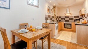 A compact kitchen with a central island, a dining area with a wooden table, and a small seating arrangement. - 1 Bed in Richmond (oc-k32861) (Richmond)