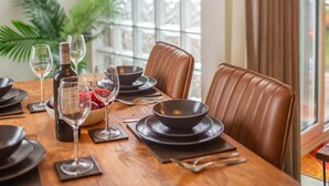 Una mesa de comedor dispuesta con platos, fuentes y cubiertos negros, junto con copas de vino y una botella de vino.