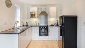 Una cocina moderna con armarios blancos, un microondas de acero inoxidable, horno empotrado, refrigerador negro y piso de madera.