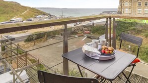 Un balcón con una mesa dispuesta para el desayuno, con vista a una carretera costera y un edificio histórico.