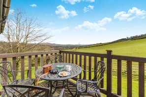A round metal table with chairs on a wooden deck, overlooking a green field and hills. - 2 Bed in Caersws (oc-waa322) (Trefeglwys)
