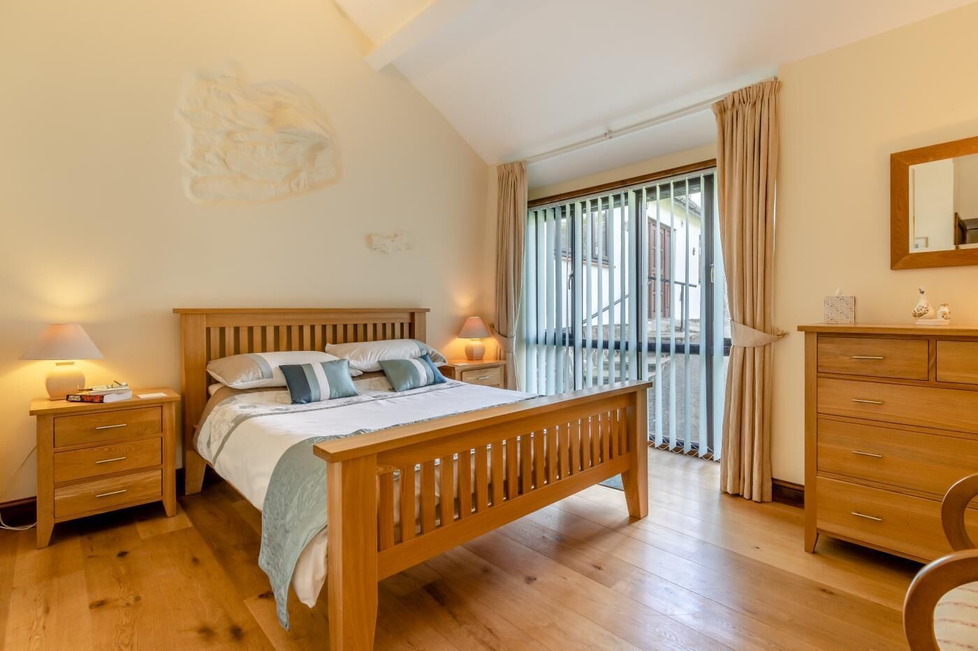 Een slaapkamer met een houten bed, nachtkastjes, een kaptafel en een balkon met gordijnen.