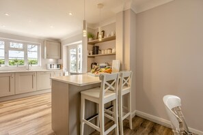 A modern kitchen with a central island, white bar stools, and a view of the outdoors. - 3 Bed in Rushmere St. Andrew (oc-1lux) (Rushmere Saint Andrew)