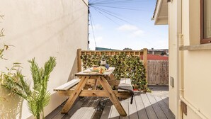 A wooden deck with a picnic table, surrounded by plants and a wooden fence. - 2 Bed in Newquay (oc-j32859) (Newquay)