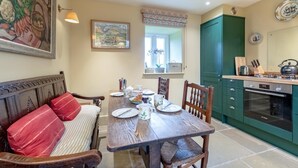 A dining area with a wooden table set for four, surrounded by chairs. A bench with red cushions is against the wall. A window with a view of greenery is above the table. - 2 Bed in Brassington (oc-dcgol) (Brassington)