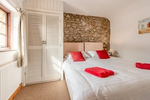 Ein Schlafzimmer mit Stehwand, einem weißen Bett mit roten Kissen und einem weißen Kleiderschrank mit Klappläden.