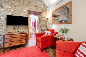 A stone-walled room with a TV, wooden furniture, and a mirror. - 2 Bed in Little Haven (oc-wav325) (Little Haven)