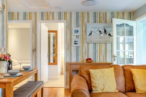 Ein Wohnzimmer mit braunem Ledersofa, einem Esstisch mit Blumenvase und einem Gemälde von Papageitauchern an der Wand.