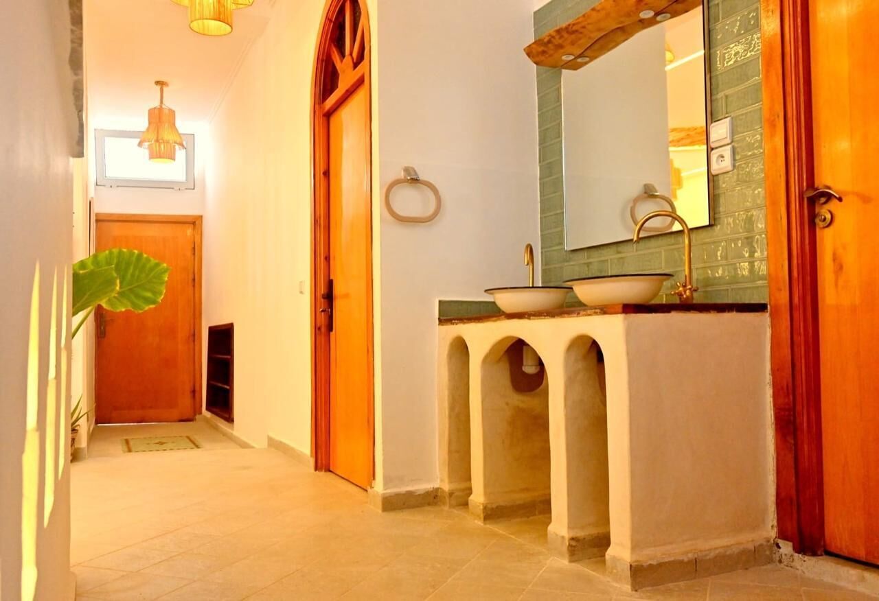 A hallway with a wooden door, a sink with a green backsplash, and a mirror above it.