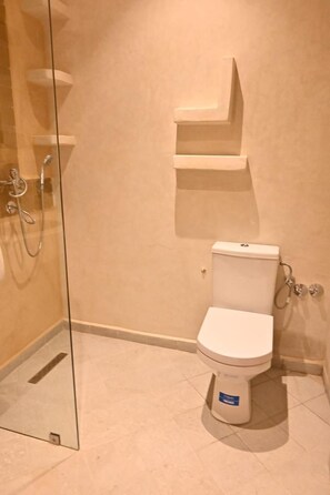 A bathroom with a glass shower enclosure, a white toilet, and a small shelf above the toilet. - RAYAN HOUSE (Tamraght)