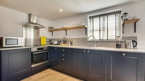 A modern kitchen with dark cabinets, a microwave, oven, and a window with blinds. - 1 Bed in Holt (oc-2184) (Holt)