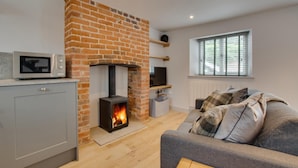 A cozy living room with a fireplace, a grey sofa, a television, and a microwave on the counter. - 1 Bed in Holt (oc-2185) (Holt)